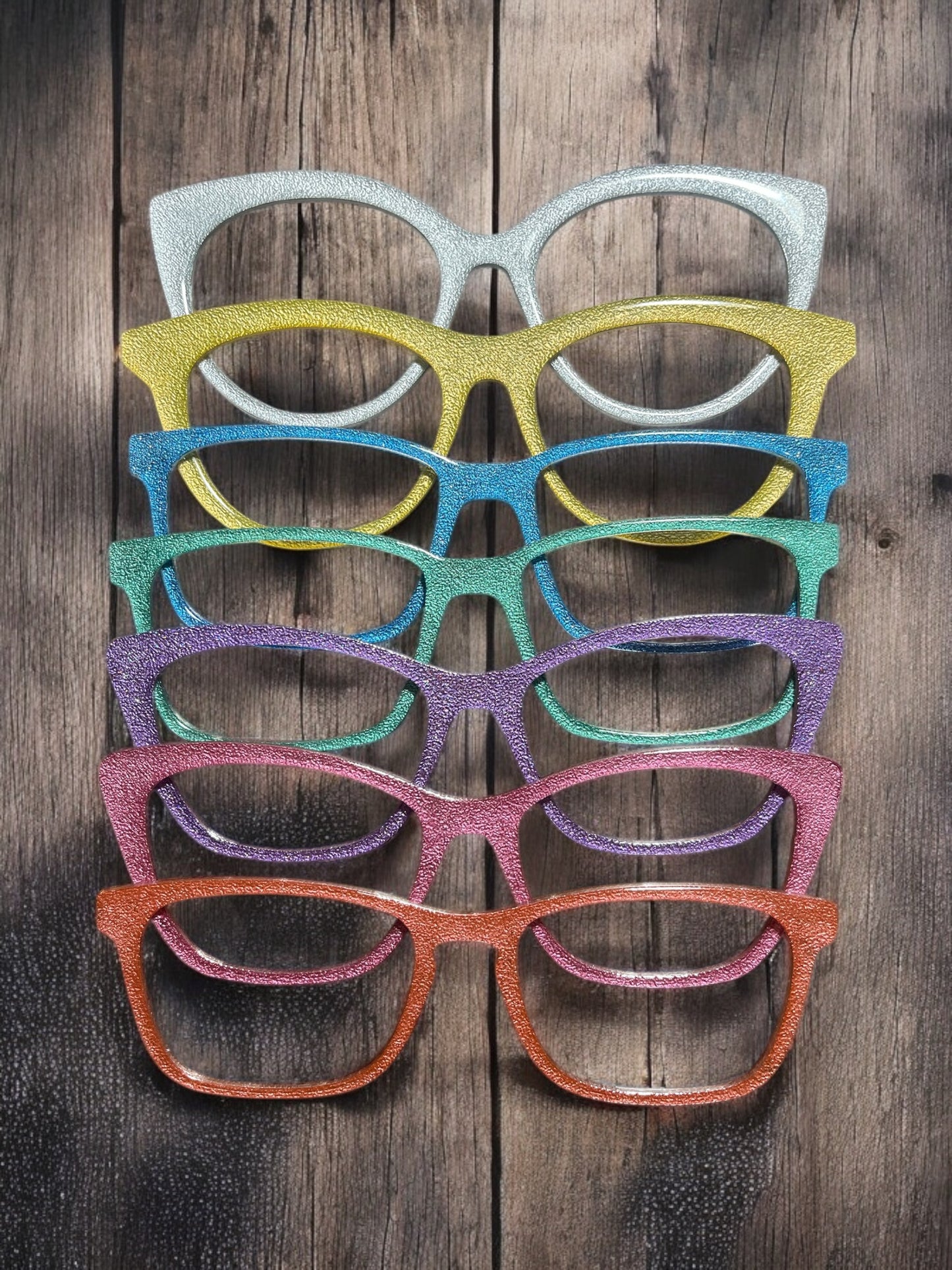 Seven colorful eyeglass frames hang in a row on a rustic wooden wall. 
